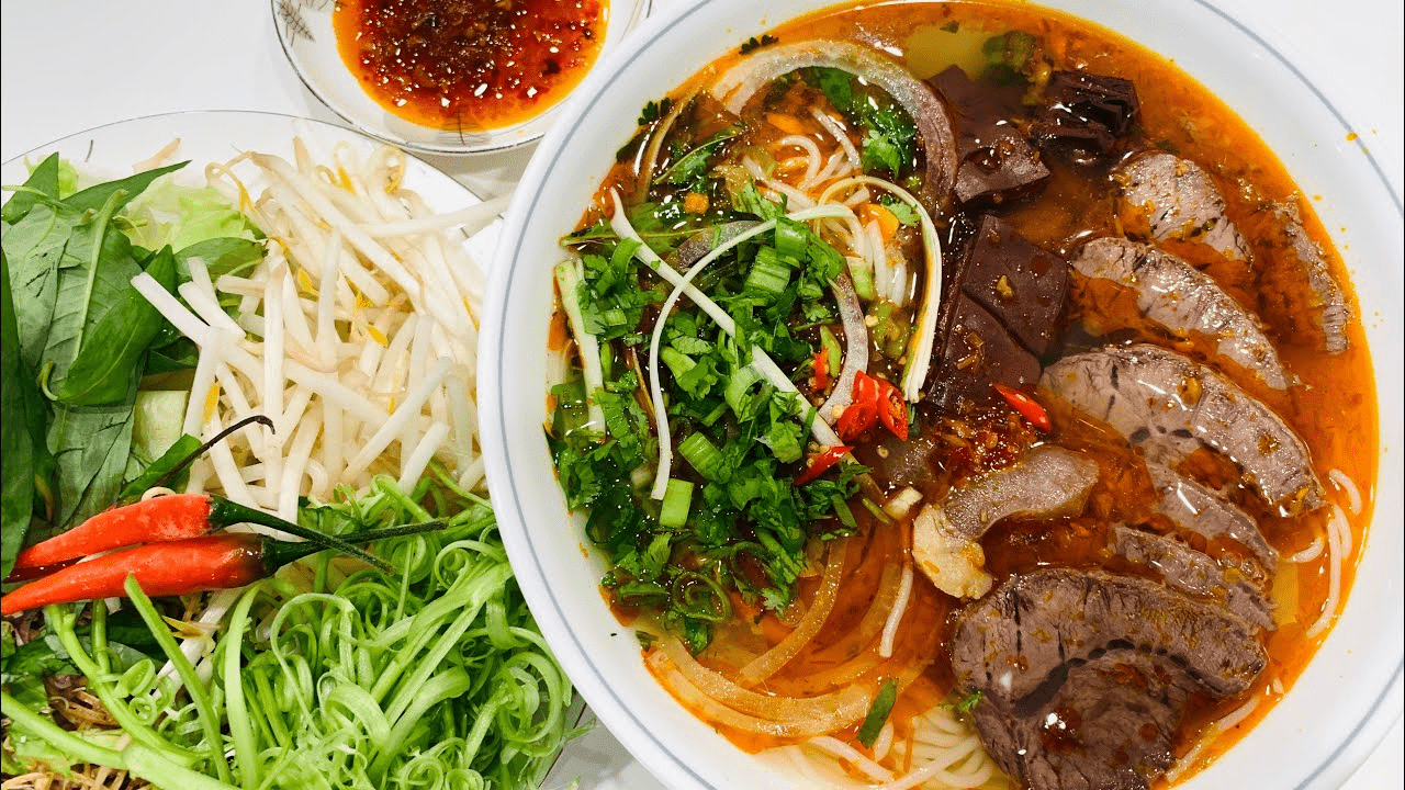 A bowl of Bun Bo Hue with beef slices, herbs, and spicy broth