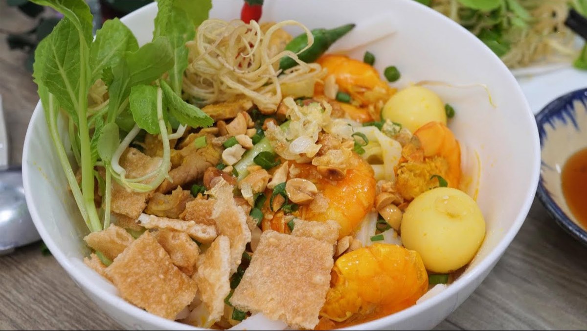 Bowl of Mi Quang noodles with shrimp, pork, herbs, and rice crackers