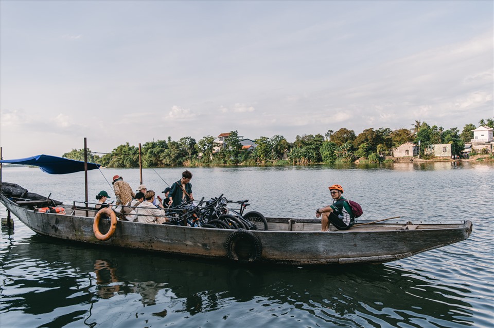 Visitors cycling across a bridge and taking a boat ride to reach a riverside craft village