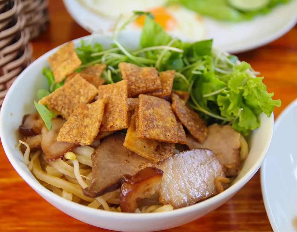 Local food in hoi An - A mouthwatering bowl of Cao Lau, featuring thick noodles, tender pork slices, fresh greens, and crispy rice crackers.