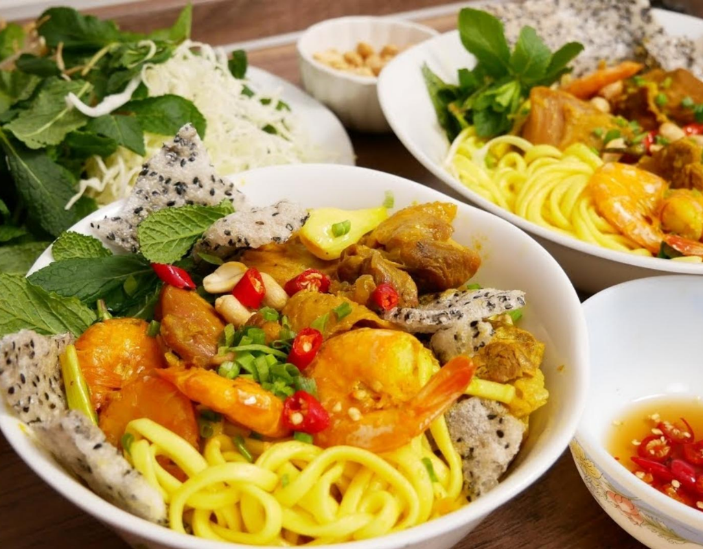 Mi Quang – A flavorful Central Vietnamese noodle dish with rich broth, herbs, peanuts, and crispy rice crackers.