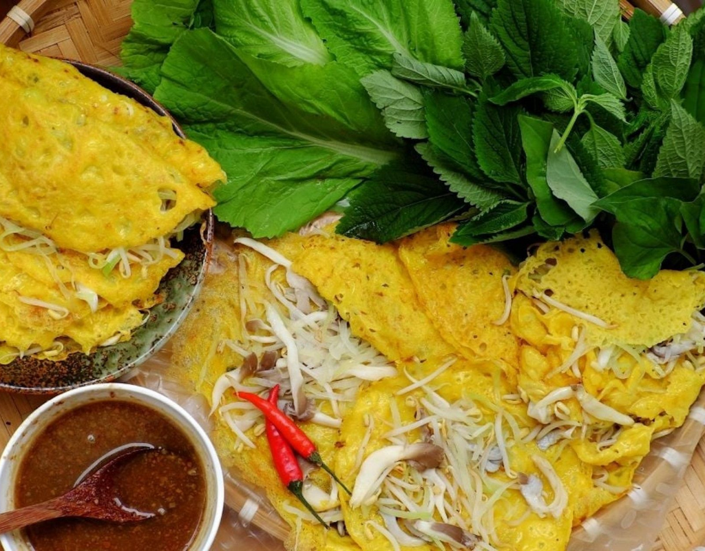 Banh Xeo – Crispy Vietnamese savory pancakes filled with shrimp, pork, and bean sprouts, served with fresh herbs.